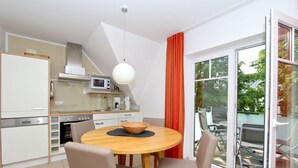 A modern kitchen with white cabinets, a microwave, and a coffee maker. There is a dining area with a round table and chairs. - Beachfront vacation rental with a balcony, access to the pool and sauna - Rex Rugia H-1010 - (Göhren)