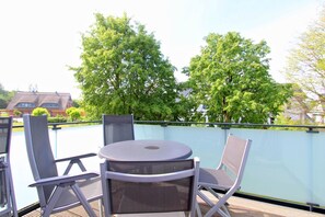 Ein Balkon mit rundem Tisch und zwei Stühlen, umgeben von einer Glasreling.