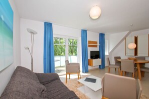 Ett modernt vardagsrum med en grå soffa, ett litet vitt bord och en matplats med ett träbord och stolar.