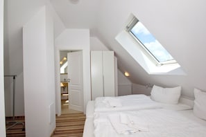 Un dormitorio con tragaluz, una cama, un armario y un baño visible a través de una puerta abierta.
