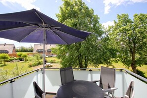 A balcony with a table and chairs, an umbrella, and a view of a garden and buildings. - Beachfront vacation rental with a balcony, access to the pool and sauna - Rex Rugia H-1010 - (Göhren)