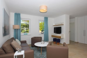 A modern living room with a sofa, a coffee table, a TV, and a small dining area.