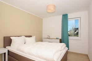 Une chambre à coucher avec un lit, une table de chevet, une fenêtre avec des rideaux et un luminaire au plafond.