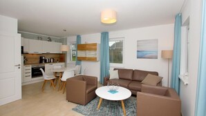A modern apartment with a living room, dining area, and kitchen. There is a brown sofa set, a round coffee table, and a dining table with chairs. - Beachfront apartment with terrace, use of swimming pool and sauna - Rex Rugia H-1010 - (Göhren)