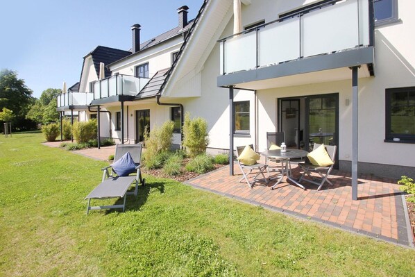 A modern two-story house with a patio area featuring outdoor furniture and a small table.