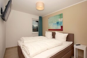 A hotel room with a bed, a TV mounted on the wall, a window with curtains, and a painting above the bed. - Beachfront vacation rental with a terrace, access to the pool and sauna - Rex Rugia - Rex (Göhren)