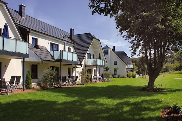 A row of modern houses with balconies, a grassy lawn, and a tree.