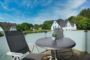 A balcony with a round table and chairs, a potted plant, and a view of houses in the background. - Beachfront vacation rental with a balcony, access to the pool and sauna - Rex Rugia H-1010 - (Göhren)