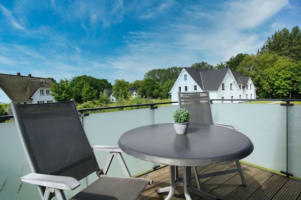 A balcony with a round table and chairs, a potted plant, and a view of houses in the background.
