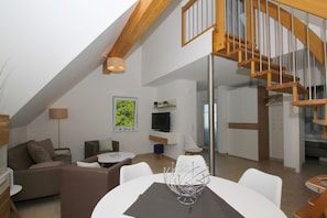 A modern loft apartment with a high ceiling, exposed wooden beams, a staircase, a dining area, and a living room with a TV and seating. - Beachfront vacation rental with a balcony, access to the pool and sauna - Rex Rugia - Rex Rugia (Göhren)