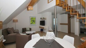 A modern loft apartment with a high ceiling, exposed wooden beams, a staircase, a dining area, and a living room with a TV and seating. - Beachfront vacation rental with a balcony, access to the pool and sauna - Rex Rugia H-1010 - (Göhren)