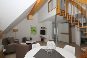 Un loft moderno con techos altos, una escalera de madera, un comedor y una sala de estar con televisor de pantalla plana.
