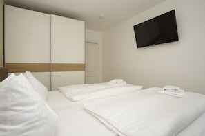 A hotel room with two beds, a TV mounted on the wall, and a wardrobe with a mirror.