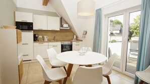 A modern kitchen with white cabinets, a dining table with chairs, and a view through the glass door. - Beachfront vacation rental with a balcony, access to the pool and sauna - Rex Rugia H-1010 - (Göhren)