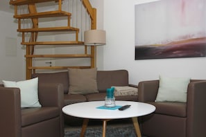 A living room with a round white table, brown leather sofas, a wooden spiral staircase, and a painting on the wall.