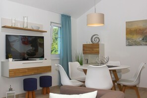 A modern living room with a flat-screen TV, a dining area with white chairs, a round table, and a blue curtain. - Apartment close to the beach with balcony, use of swimming pool and sauna - Rex Rugia - Rex Rugia (Göhren)