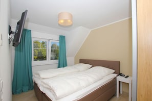 A bedroom with a bed, a bedside table, a TV mounted on the wall, and a window with curtains.