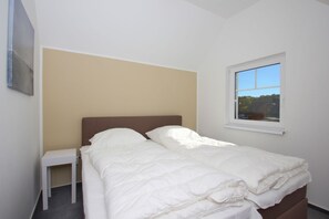 A bedroom with a bed, a nightstand, a window with a view, and a wall-mounted picture.