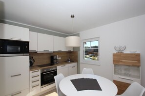 A modern kitchen with white cabinets, a microwave, stove, and a dining area with a white table and chairs.