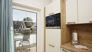 Une cuisine moderne dotée d’un four à micro-ondes encastré, de meubles en bois et offrant une vue sur une terrasse extérieure grâce à une porte vitrée.