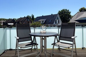 A balcony with two chairs and a table, a glass jar with stones, and a view of houses in the background. - Beachfront apartment with a balcony; access to the pool and sauna - Rex Rugia - Rex Rugia (Göhren)