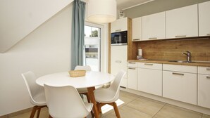 Une cuisine moderne avec des meubles blancs, un plan de travail en bois et un coin repas comprenant une table et des chaises blanches.