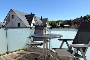 A rooftop terrace with a table and chairs, a glass partition, and a view of residential buildings.