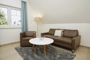 A living room with a brown sofa, a white coffee table, a floor lamp, and a window with blue curtains.