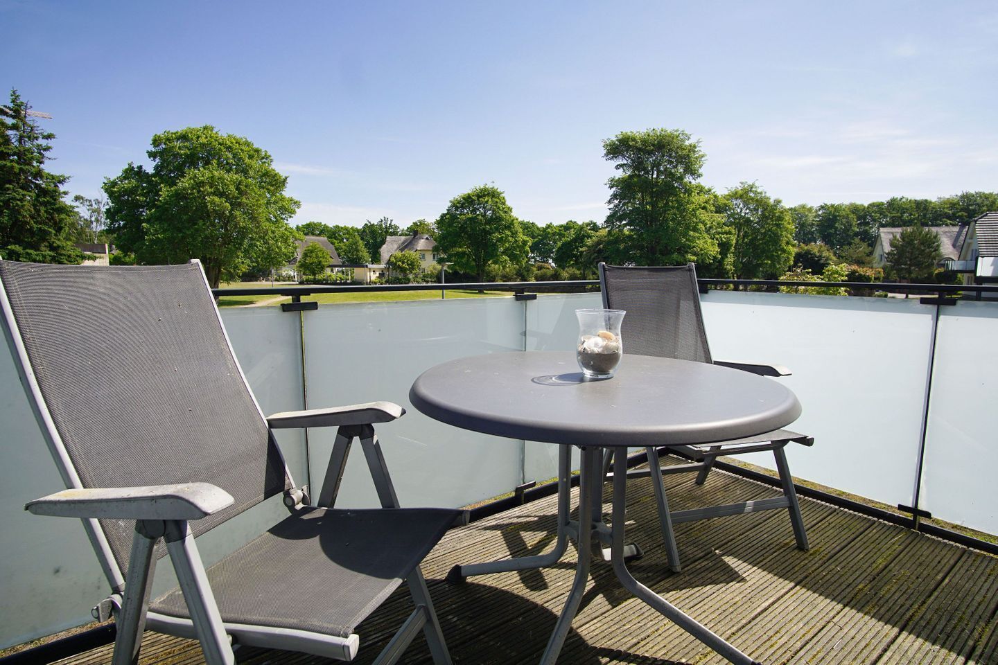 Une terrasse sur le toit avec une table ronde et deux chaises, un verre contenant une boisson, et une vue sur la verdure et les bâtiments.