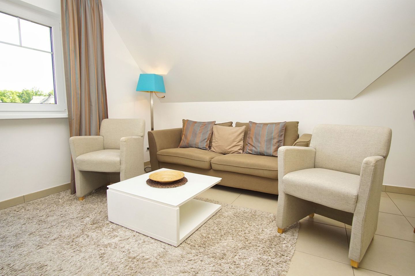 Un salon comprenant un canapé, deux fauteuils, une table basse, une lampe et une fenêtre avec des rideaux.