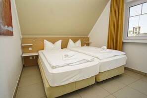 A twin bed room with a wooden headboard, a window with curtains, and a small bedside table.