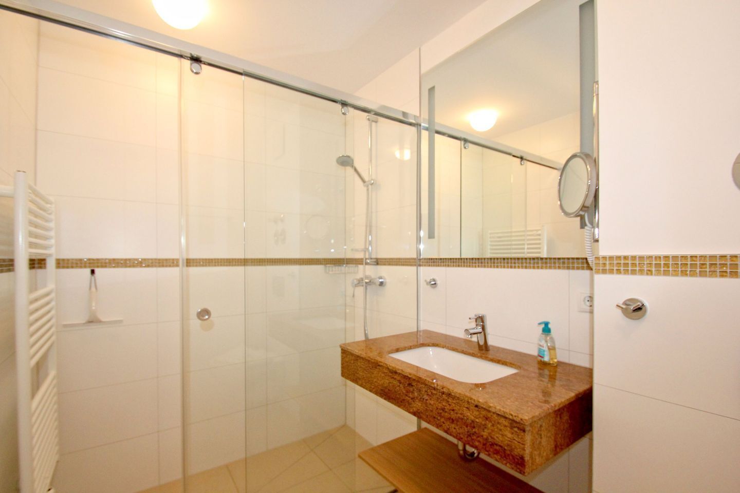 A modern bathroom with a glass-enclosed shower, a sink with a marble countertop, and a mirror above the sink.