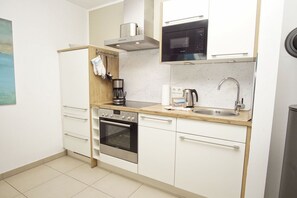 A compact kitchen with a stove, oven, microwave, sink, and a coffee maker. - Beachfront vacation rental with a terrace, access to the pool and sauna - Rex Rugia - Rex (Göhren)