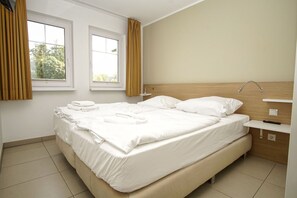 A hotel room with a large bed, two windows, a bedside table, and a nightstand. - Beachfront vacation rental with a terrace, access to the pool and sauna - Rex Rugia H-1010 - (Göhren)