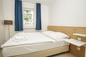 Una habitación de hotel con cama, mesita de noche, lámpara y ventana con cortinas.