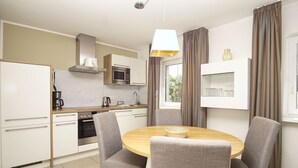 A modern kitchen with white cabinets, a microwave, and a coffee maker. There is a dining area with a round table and four grey chairs. - Beachfront vacation rental with a balcony, access to the pool and sauna - Rex Rugia H-1010 - (Göhren)