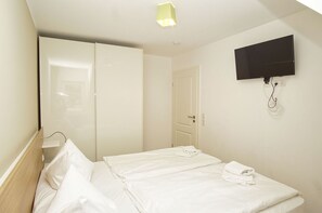 A hotel room with a bed, a TV mounted on the wall, and a door leading to another room.