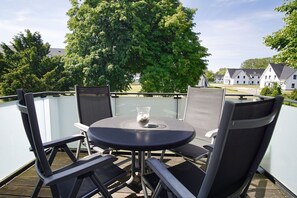 Un balcon avec une table ronde et quatre chaises, donnant sur un quartier résidentiel avec des maisons et des arbres.