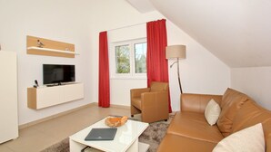 Un salon moderne avec un téléviseur à écran plat, un canapé, une table basse et une lampe.