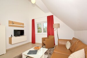 Ett modernt vardagsrum med en platt-TV, en soffa, ett soffbord och en lampa.
