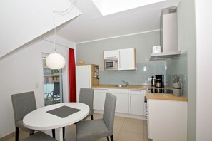 A compact kitchen with a dining area, a microwave, a coffee maker, and a red curtain. - Beachfront vacation rental with a balcony, access to the pool and sauna - Rex Rugia H-1010 - (Göhren)
