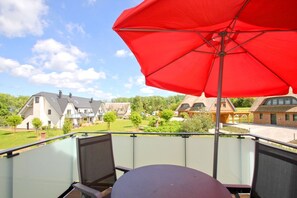 A balcony with a red umbrella, a table, and chairs.