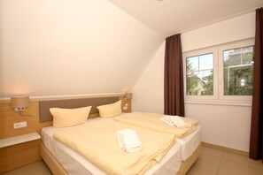 A hotel room with a bed, two bedside lamps, a window with curtains, and a view of trees outside. - Beachfront vacation rental with a balcony, access to the pool and sauna - Rex Rugia H-1010 - (Göhren)