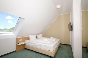 A small, modern hotel room with a sloped ceiling, a single bed, a bedside table, a TV, and a window with a view of a construction site. - Beachfront vacation rental with a balcony, access to the pool and sauna - Rex Rugia - Rex Rugia (Göhren)