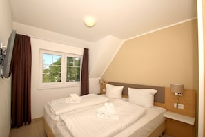 A hotel room with two beds, a window with curtains, a flat-screen TV, and a ceiling light. - Beachfront apartment with balcony, use of swimming pool and sauna - Rex Rugia apartment 14-6 - (Göhren)