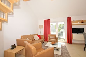 Ein modernes Wohnzimmer mit einer Couch, einem Sessel, einem Couchtisch und einem Fernseher.