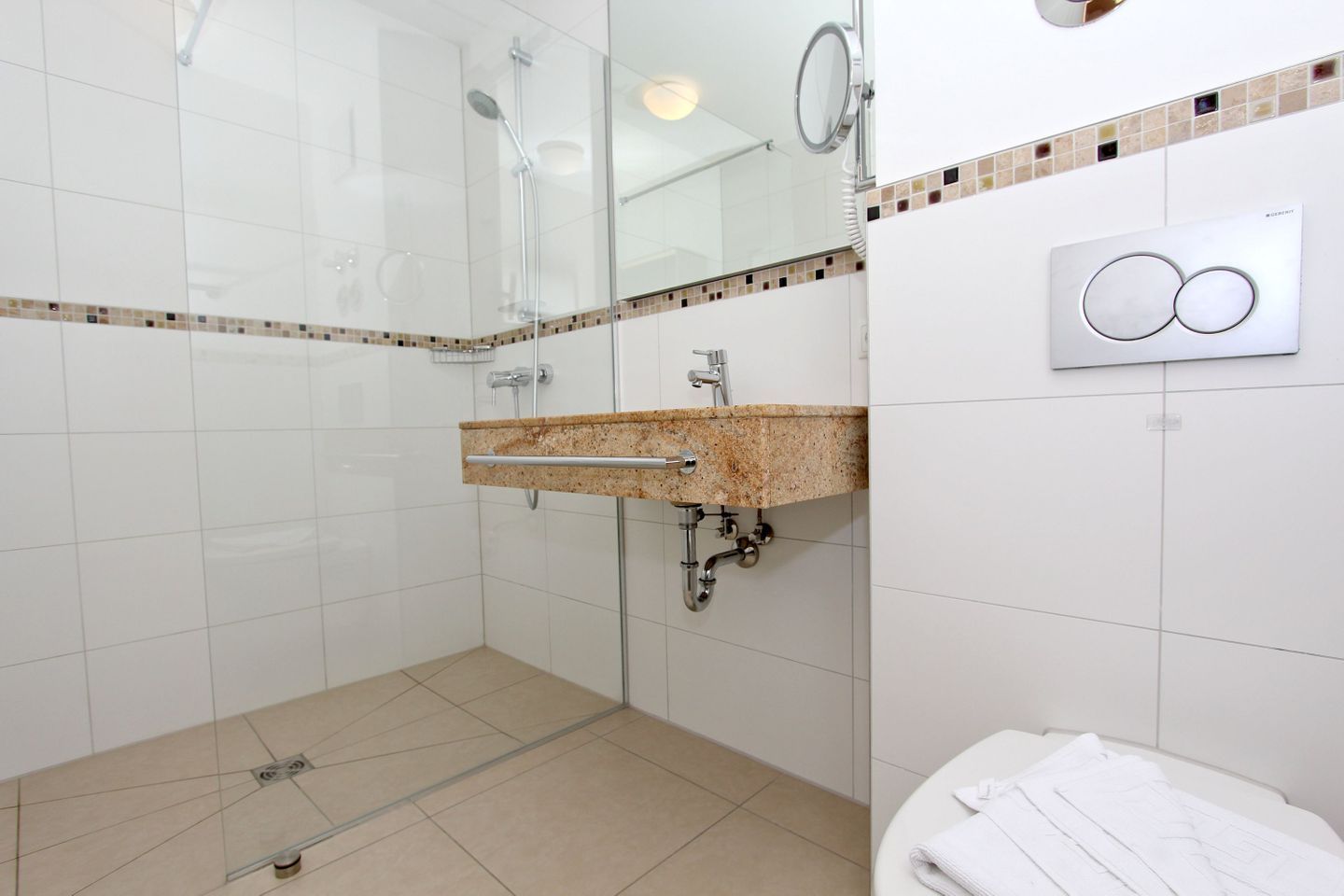 A modern bathroom with a glass shower enclosure, a granite countertop sink, and a white tiled floor.