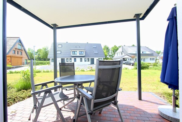 An outdoor patio with a table and chairs, a blue umbrella, and a view of houses in the background.
