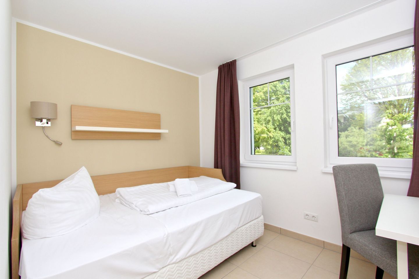 Hotelkamer met een bed, een bureau, een stoel, een wandlamp en een raam met gordijnen.