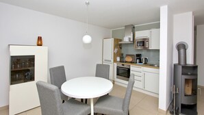 A compact kitchen with modern appliances, a dining area with grey chairs, and a wood-burning stove. - Beachfront vacation rental with a terrace, access to the pool and sauna - Rex Rugia - Rex (Göhren)